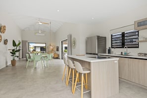 A modern kitchen with a central island, bar stools, and a dining area with a green table and chairs. - Villa Santi Mambo Beach With Privatepool (Willemstad)