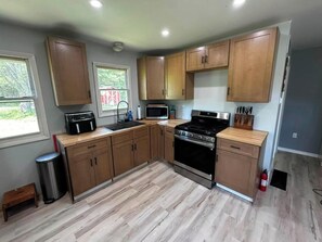 A kitchen with wooden cabinets, a stove, a microwave, and a trash can. - Home Away From Home (Franklinville)