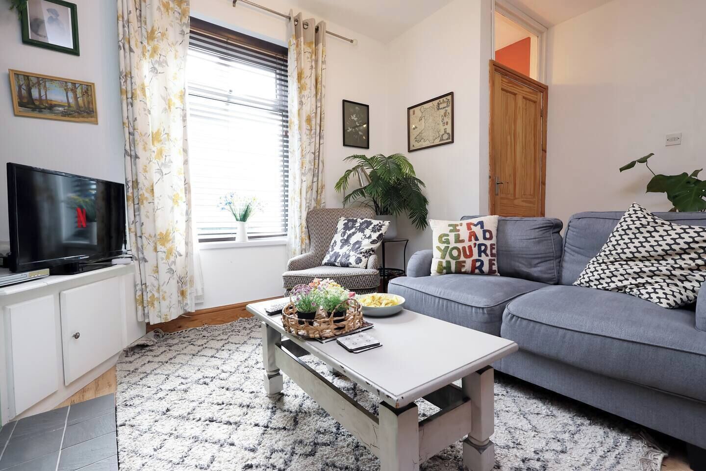 A living room with a sofa, a coffee table, a television, and a window with curtains.