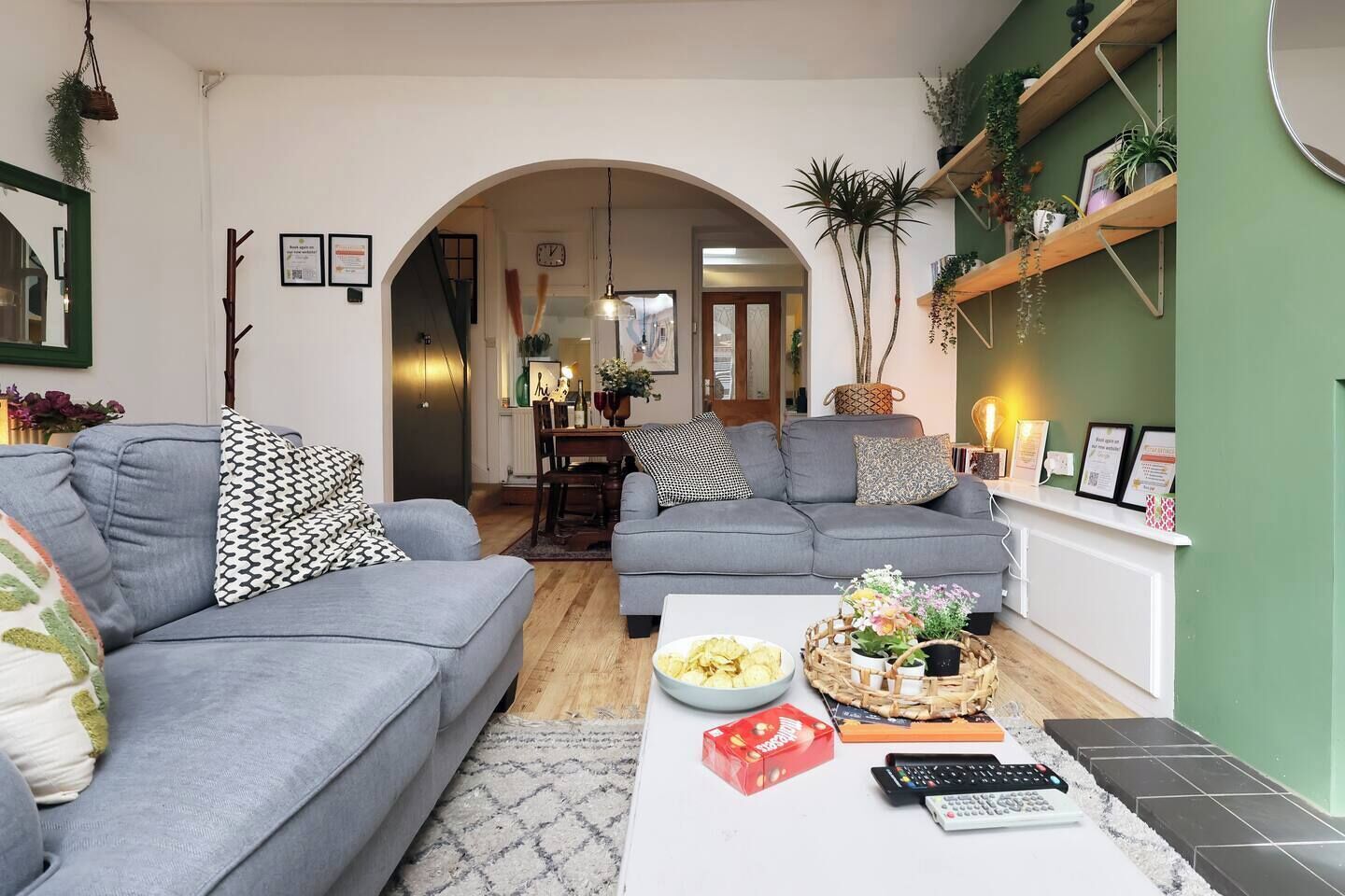 A living room with two grey sofas, a coffee table with snacks, and a bookshelf with plants.