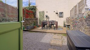 A patio area with a table and chairs, a stone wall, and a wooden bench. - #02 Just the Splott! Sleeps 6, 8mins to Stadium. (Cardiff)