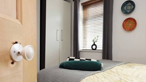A bedroom with a bed, a window with blinds, a door with a handle, and a wall with two decorative plates. - #02 Just the Splott! Sleeps 6, 8mins to Stadium. (Cardiff)