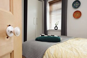 Ein Schlafzimmer mit einem Bett, einem Fenster mit Jalousien, einer Tür mit Griff und einer Wand mit zwei dekorativen Tellern.