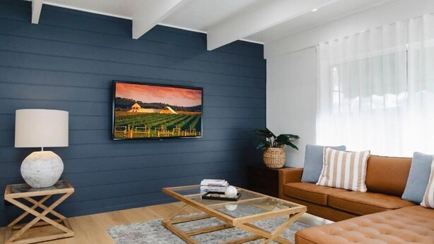 A modern living room with a dark blue wall, a glass coffee table, a brown sofa, and a painting of a vineyard. - 9 Anne St Diamond Cr (Diamond Creek)