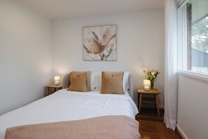 A bedroom with a bed, two bedside tables with lamps, a window, and a wall-mounted artwork. - 9 Anne St Diamond Cr (Diamond Creek)