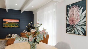 A modern living room with a dining table, a sofa, a TV mounted on the wall, and a large floral painting. - 9 Anne St Diamond Cr (Diamond Creek)