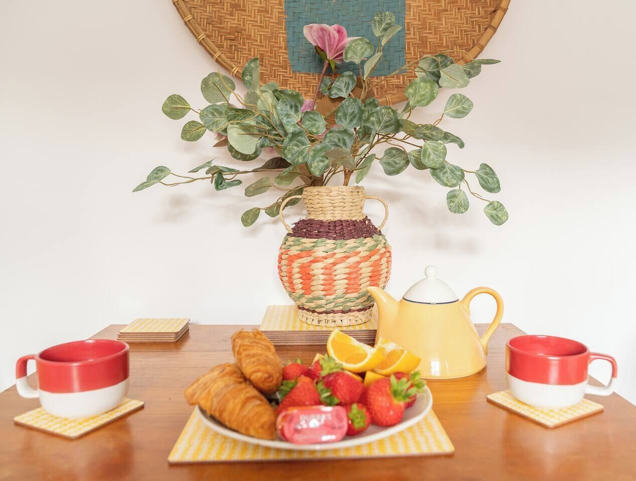 Une table dressée avec une théière, des tasses, une assiette de pâtisseries et une plante en pot.