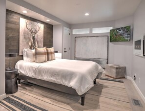A modern bedroom with a large bed, a wall-mounted artwork of a deer head, and a large window. - Mountain Modern Condo | AC, Pool, Hot Tub, Golf & Ski (Durango)