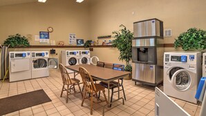 A laundry facility with multiple washing machines, a water cooler, and a dining area with chairs and a table. - Mountain Modern Condo | AC, Pool, Hot Tub, Golf & Ski (Durango)