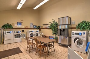 A laundry facility with multiple washing machines, a water cooler, and a dining area with chairs and a table. - Mountain Modern Condo | AC, Pool, Hot Tub, Golf & Ski (Durango)