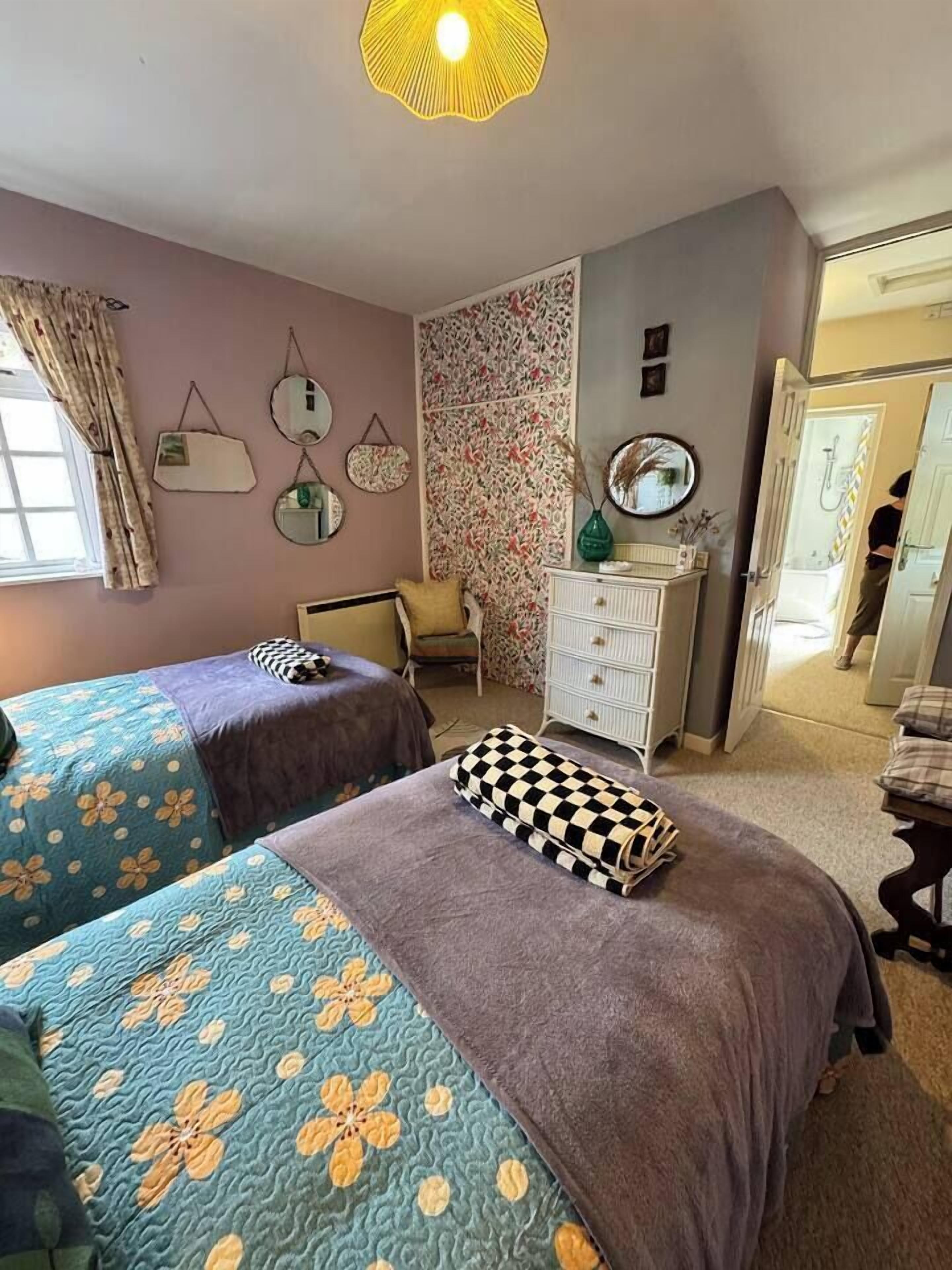 A bedroom with two beds, a dresser, a chair, and a mirror on the wall.