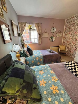 A room with two beds, a chair, a lamp, and a window with curtains.