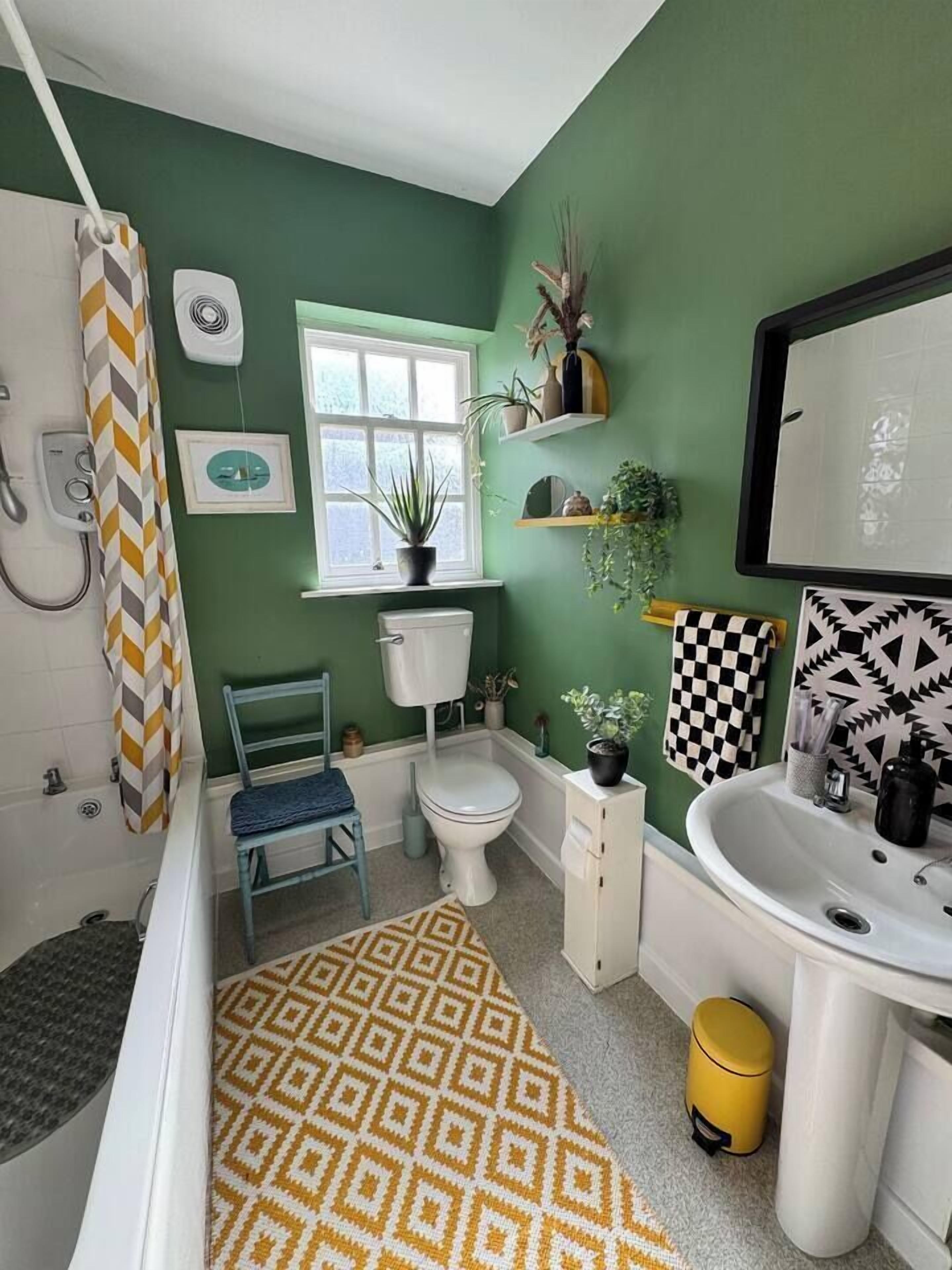 A bathroom with a green wall, a white toilet, a white sink, a shower, and a patterned rug.