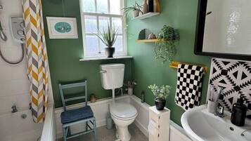 A bathroom with a green wall, a white toilet, a white sink, a shower, and a patterned rug.