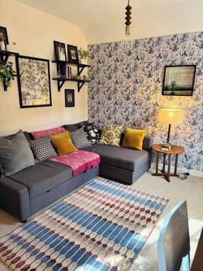 A living room with a grey sofa, patterned rug, and a wall with floral wallpaper.