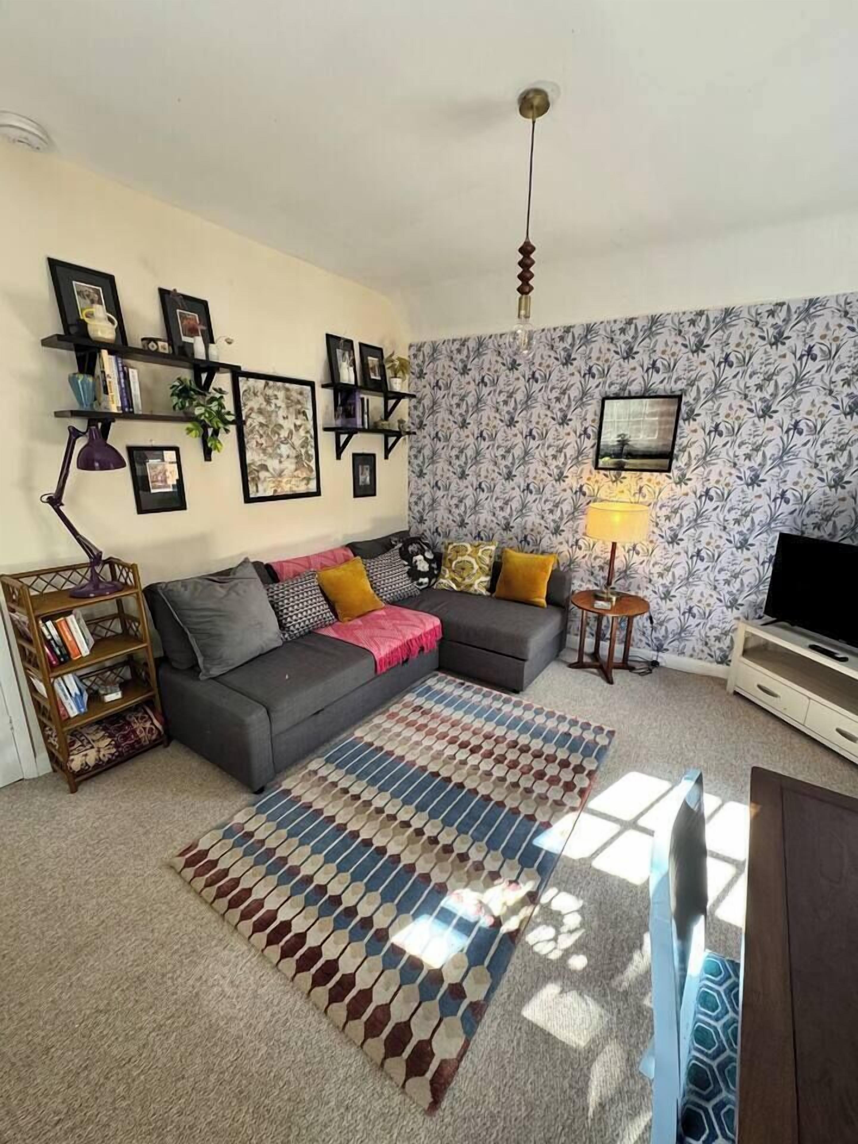 A living room with a sofa, a coffee table, a TV, and a patterned rug.