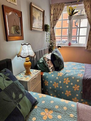 Une chambre avec deux lits, une table de chevet avec une lampe, une commode et une fenêtre avec des rideaux.