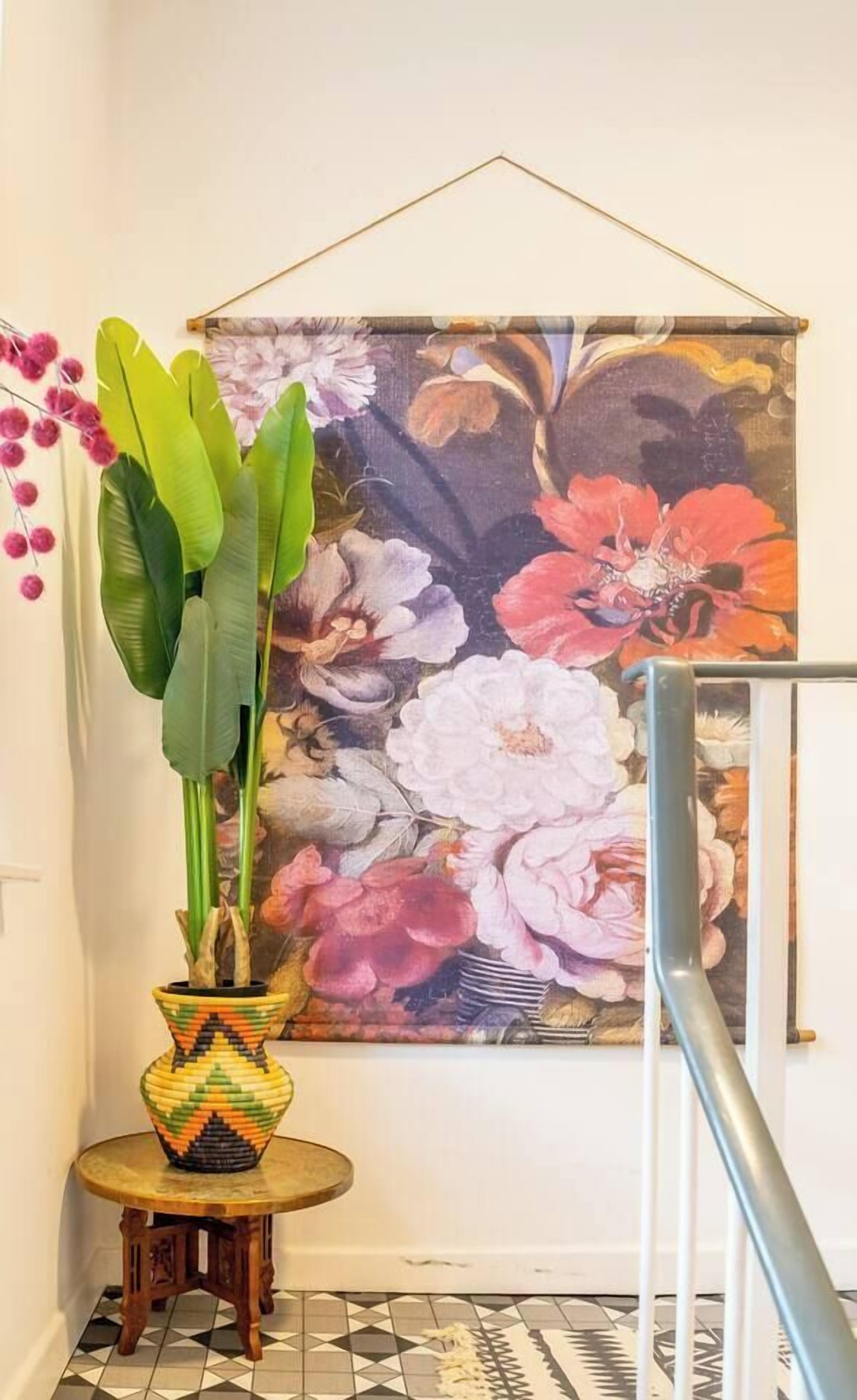 A hallway with a large floral painting, a potted plant, and a patterned floor.
