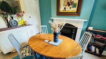 A dining area with a round wooden table, four chairs, a blue rug, a white door, a bookshelf, and a framed picture on the wall.