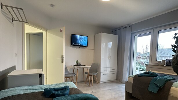 A hotel room with a bed, a desk, a television, and a view of the outside. - Cozy vacation rental for workers: Sleeps 4, 2 bedrooms, kitchen, bathroom, balcony (Hopsten)