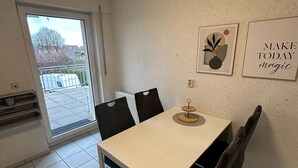A dining area with a table, chairs, a radiator, a window, and two wall decorations. - Cozy vacation rental for workers: Sleeps 4, 2 bedrooms, kitchen, bathroom, balcony (Hopsten)