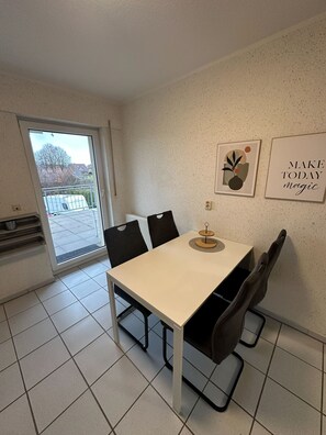 Ein Essbereich mit Tisch, Stühlen, einem Heizkörper, einem Fenster und zwei Wandbildern.