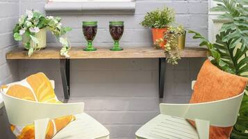 A small outdoor seating area with two chairs and a table, a window, and potted plants.