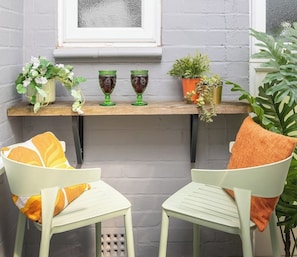 Un petit espace extérieur aménagé avec deux chaises et une table, une fenêtre et des plantes en pot.