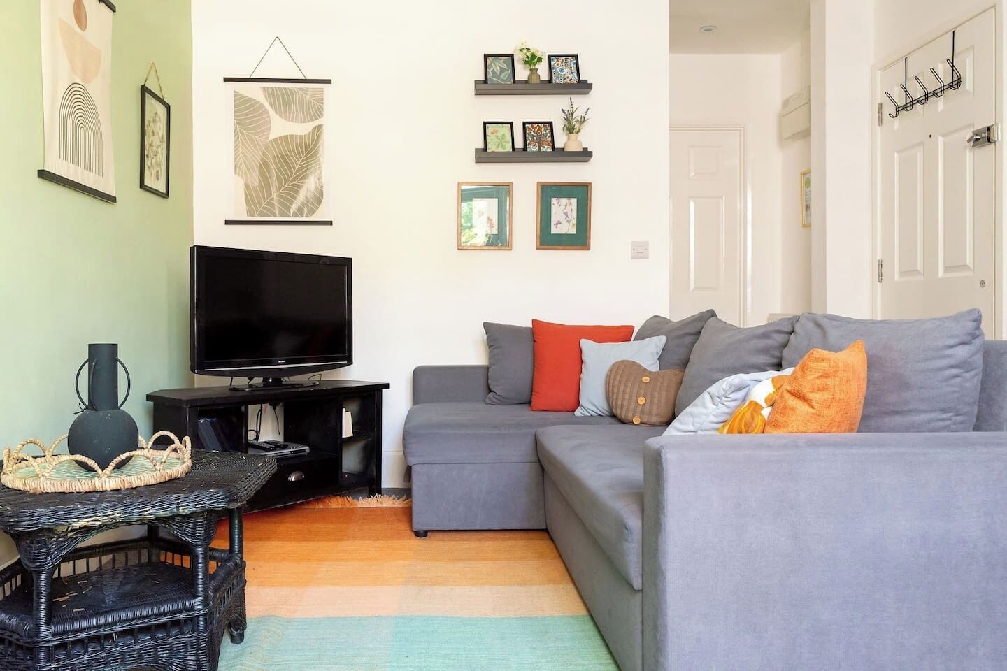 A living room with a grey sofa, a flat-screen TV, and a decorative wall with framed pictures and shelves.