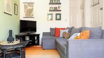 A living room with a grey sofa, a flat-screen TV, and a decorative wall with framed pictures and shelves.
