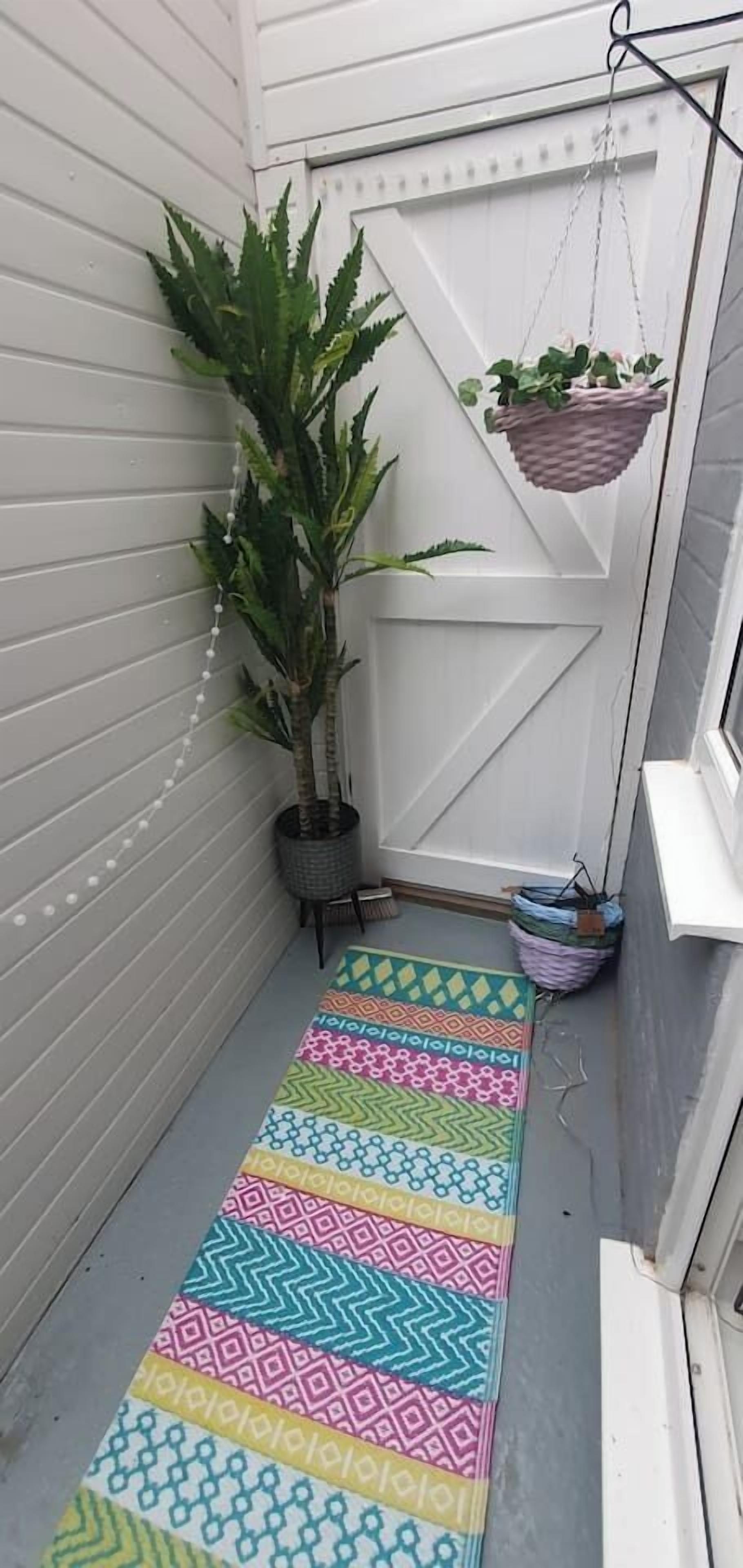 Un étroit couloir extérieur agrémenté d’un tapis à motifs, d’une plante en pot et d’une jardinière suspendue.
