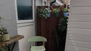 Een klein terras buiten met een groene stoel, een tafeltje en een kleurrijk vloerkleed.