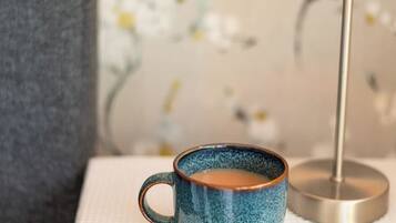 Une tasse en céramique bleue posée sur une surface blanche texturée, une lampe rose et un mur recouvert d’un papier peint à motifs floraux.