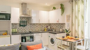 Een compacte keuken met een eethoek, een wasmachine en een bank met kussens.