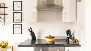 A modern kitchen with white cabinets, a stainless steel range hood, a coffee machine, and a bowl of fruit on the counter. - #09 Modern 2 bed Apart| Sleeps 5| near BHX NEC (Shirley)