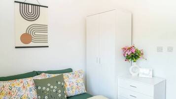 Ein Schlafzimmer mit Bett, Kleiderschrank, Nachttisch mit Blumenvase und einem an der Wand hängenden abstrakten Kunstwerk.