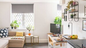 A modern living room with a sofa, a television, a dining area with a table and chairs, and a kitchen area with a stove. - #09 Modern 2 bed Apart| Sleeps 5| near BHX NEC (Shirley)