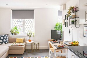 Ein modernes Wohnzimmer mit Sofa, Fernseher, Essbereich mit Tisch und Stühlen sowie Küchenzeile mit Herd.