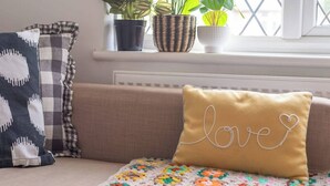 A sofa with a yellow pillow with 'love' embroidered on it, a checkered pillow, and a crocheted blanket. - #09 Modern 2 bed Apart| Sleeps 5| near BHX NEC (Shirley)