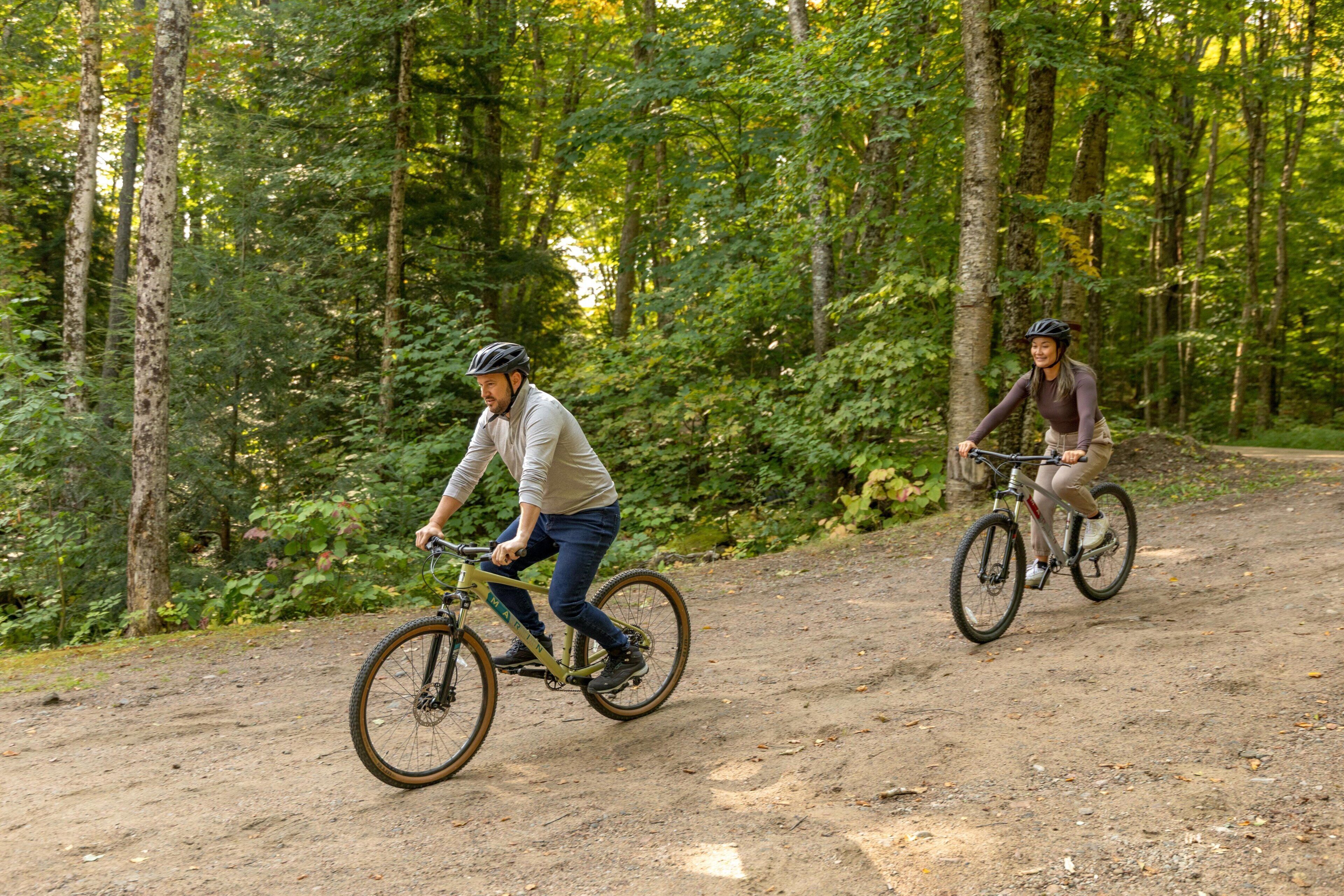 Two cyclists on a dirt path surrounded by trees.