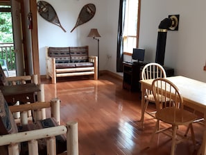 Una habitación con piso de madera, un sofá, una mesa con sillas, una lámpara y un televisor.
