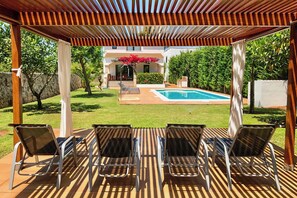 A covered outdoor area with a pool, lounge chairs, and a view of a house. - Ses Carpinyetes - Four Bedroom Villa, Sleeps 8 (Ciutadella de Menorca)