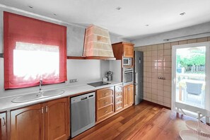 A modern kitchen with wooden cabinets, a stainless steel dishwasher, and a built-in oven. - Ses Carpinyetes - Four Bedroom Villa, Sleeps 8 (Ciutadella de Menorca)