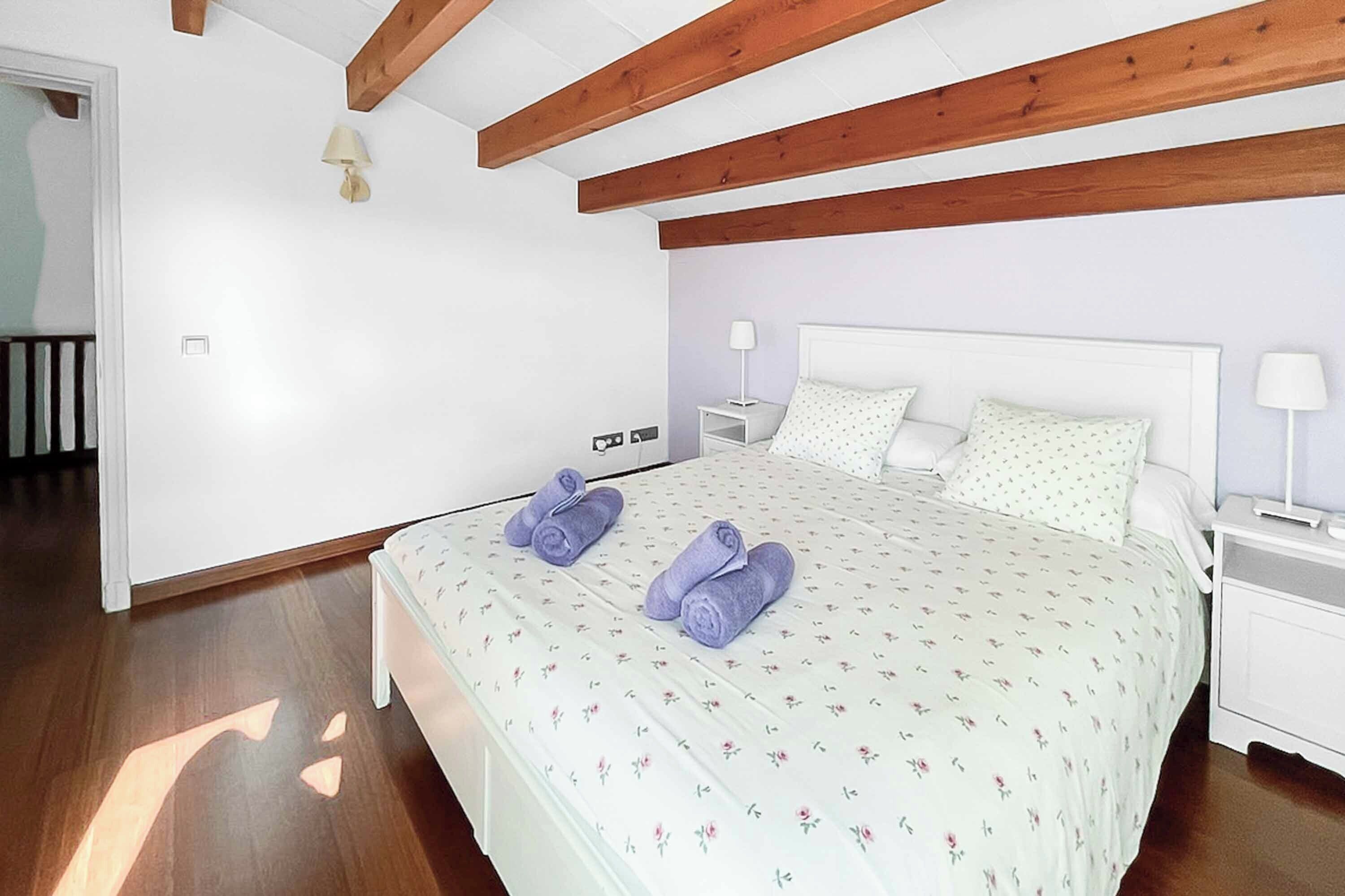 A bedroom with a bed, two nightstands, a lamp, and a wooden ceiling.