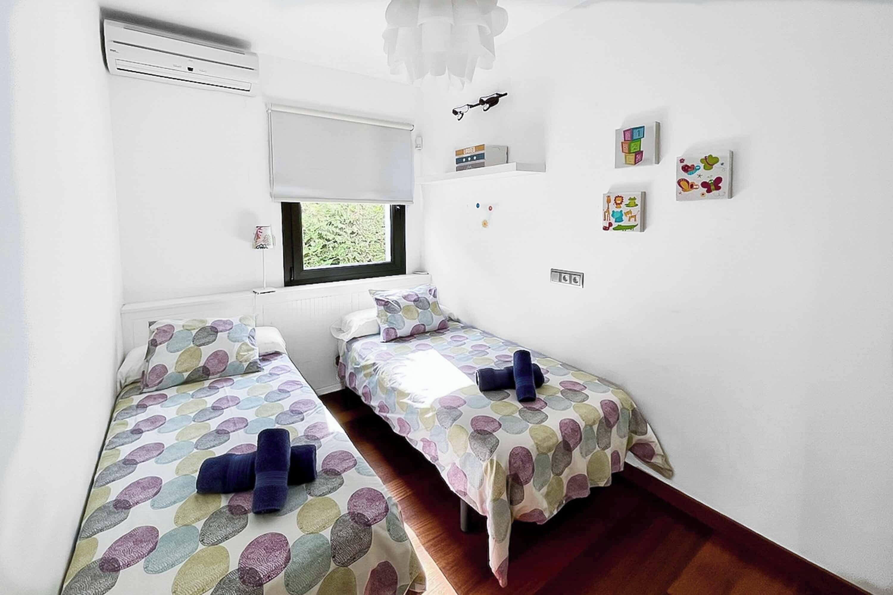 Un dormitorio con dos camas individuales, una ventana, un radiador y un aire acondicionado instalado en la pared.