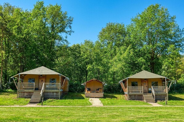 Three wooden cabins with external staircases, set in a grassy area with dense trees in the background.