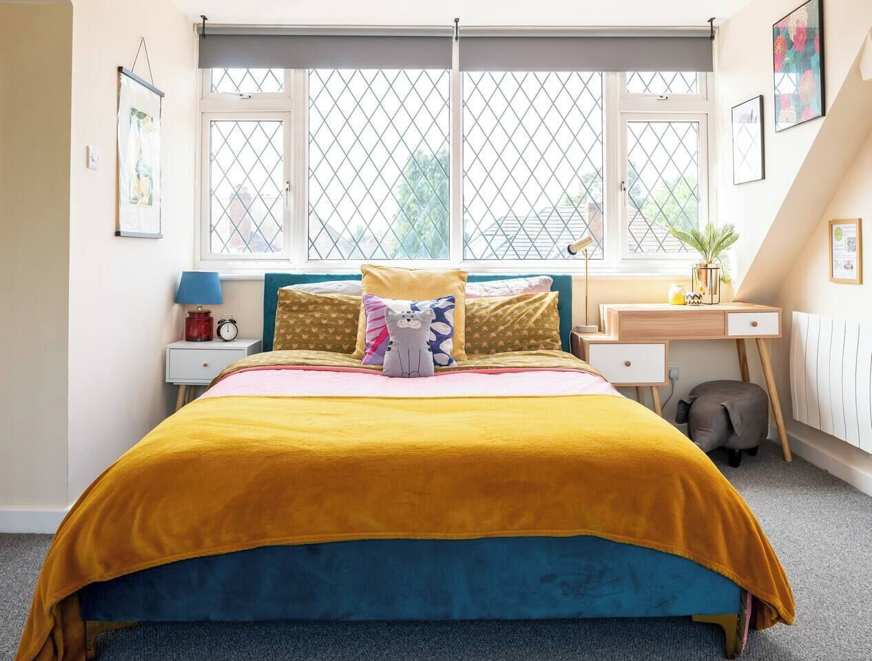 Quarto com cama, mesa de cabeceira, abajur e janela com persianas.