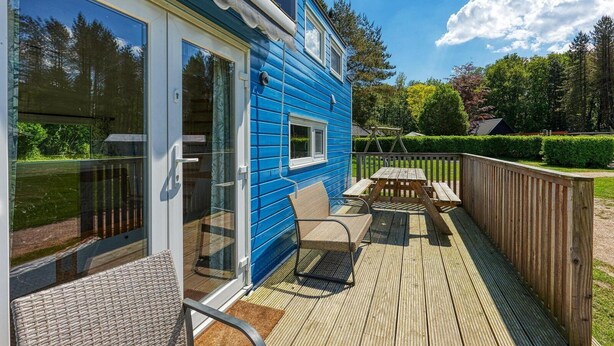 Een blauw huis met een terras, een glazen deur en een tafel met stoelen.