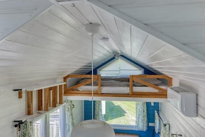 A loft bedroom with a sloped ceiling, a dormer window, and a built-in air conditioning unit. - De Glamping - Blue Tiny House | Sleeps 6 (Zeewolde)