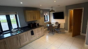 A modern kitchen with a dining area, a flat-screen TV mounted on the wall, and a large window providing natural light.